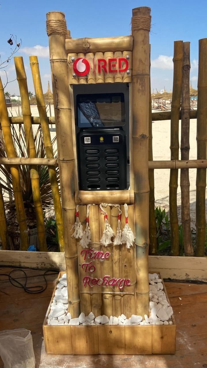 A bamboo charging station with a red neon sign on a beach deck, bamboo fencing and sand behind