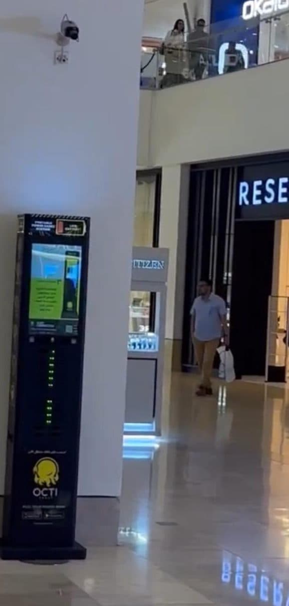 A black charging station on a mall concourse with shopfronts either side