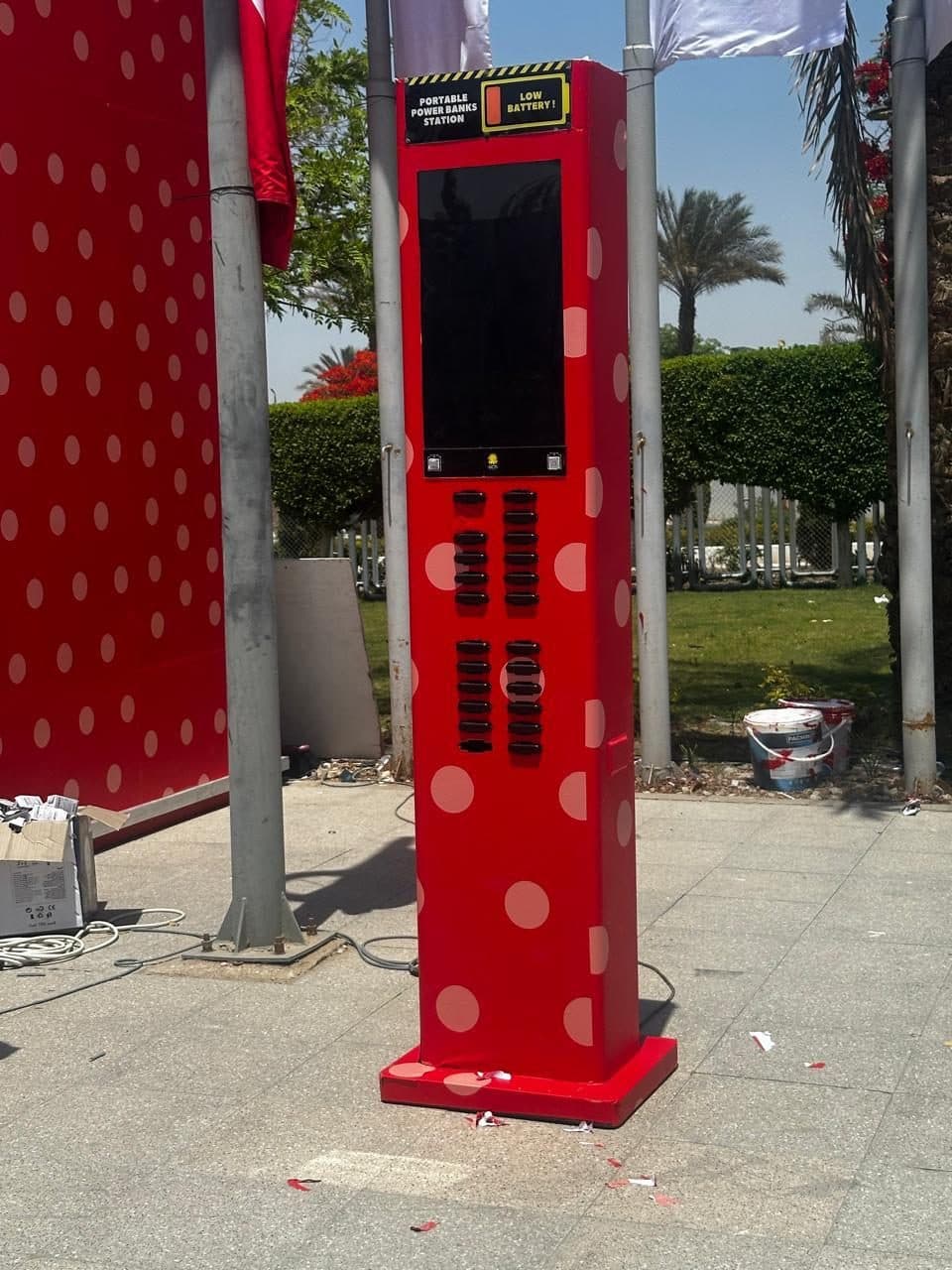 A red polka-dot charging station outdoors among flags and palm trees