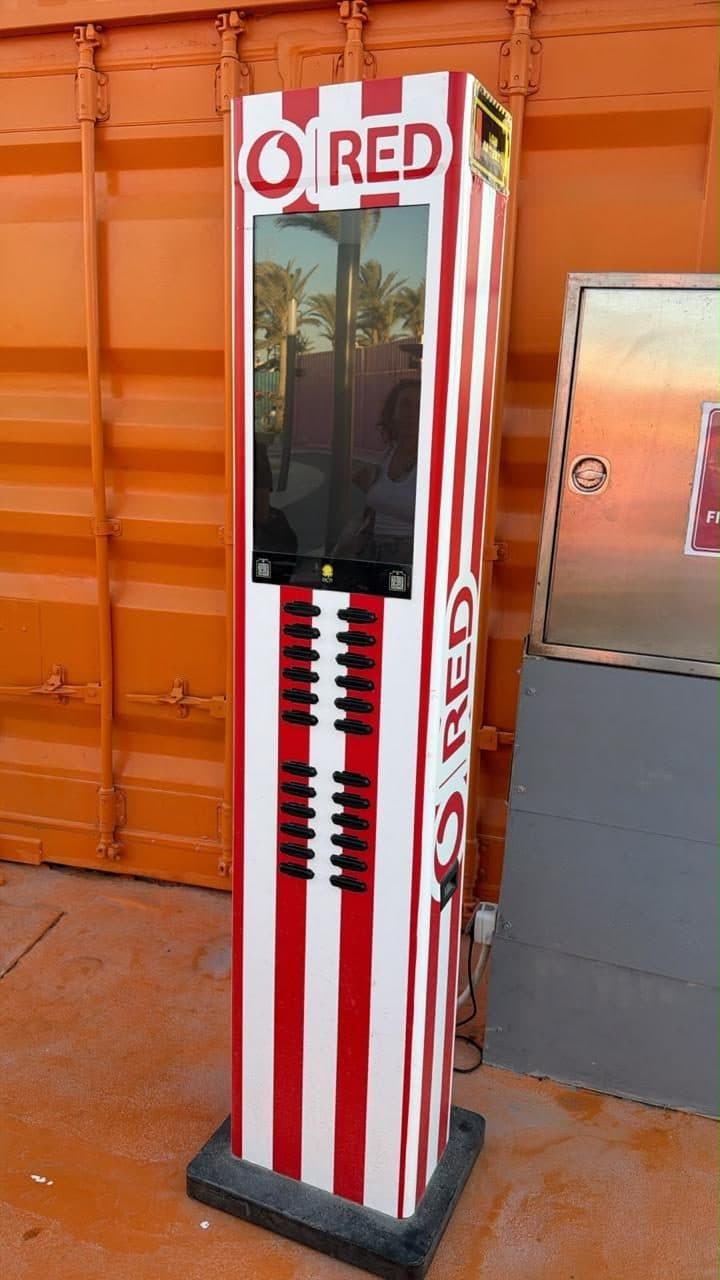 A red-and-white striped charging station standing beside an orange shipping container before installation
